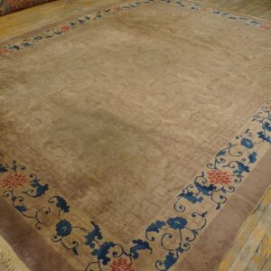 Tan rug with subtle low-pile geometric patterns and a wide border of blue and red florals on wood floorboards.
