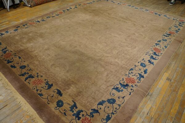 Tan rug with subtle low-pile geometric patterns and a wide border of blue and red florals on wood floorboards.
