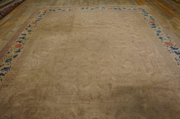 Large tan rug featuring a faint center pattern and a border with vibrant blue and red floral designs on wood.