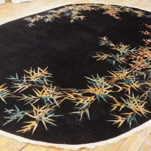 Black oval rug with yellow and teal bamboo pattern and coral flowers displayed on light wood floor.