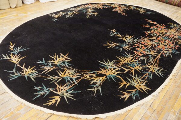 Black oval rug with yellow and teal bamboo pattern and coral flowers displayed on light wood floor.