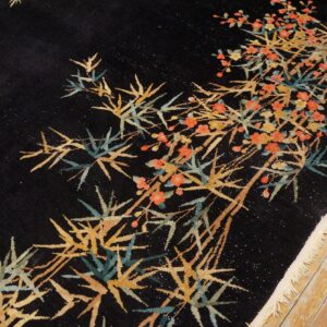 Round black rug with a pattern of golden bamboo and small orange flowers rests on light wood flooring.