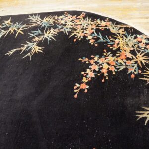 Black round rug with bamboo and coral floral designs sits on light wood flooring.