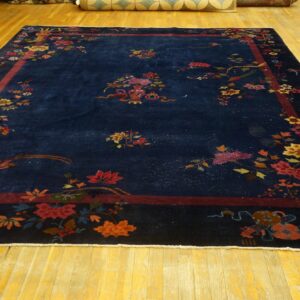Large blue rug displays scattered colorful blossoms and birds, framed by a thick burgundy border on wood floors.