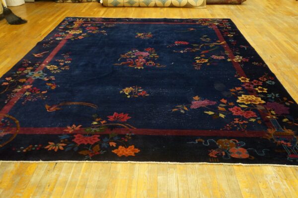 Large blue rug displays scattered colorful blossoms and birds, framed by a thick burgundy border on wood floors.