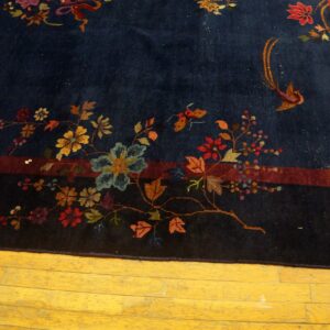 Navy rug with intricate red, blue, and gold floral and bird patterns on a yellow hardwood floor.