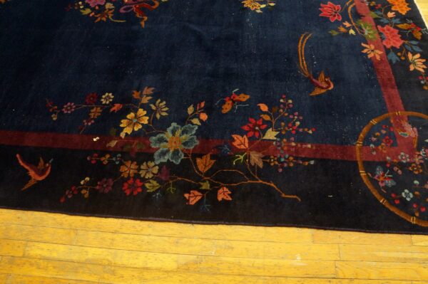 Navy rug with intricate red, blue, and gold floral and bird patterns on a yellow hardwood floor.