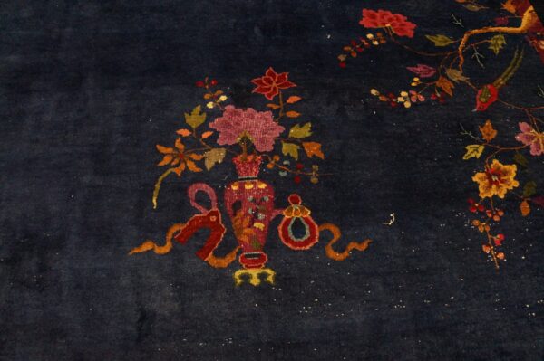 Detail of a dark blue rug with intricate floral arrangements, ribbons, and a bird motif.