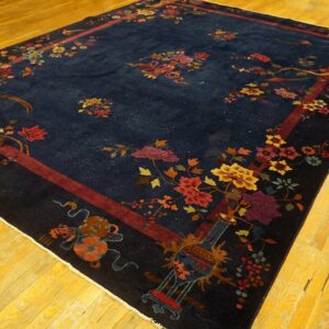 Navy blue rug with multicolored floral and figural motifs, framed by a maroon border on yellow wood flooring.