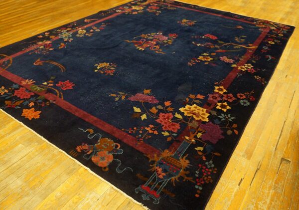 Navy blue rug with multicolored floral and figural motifs, framed by a maroon border on yellow wood flooring.