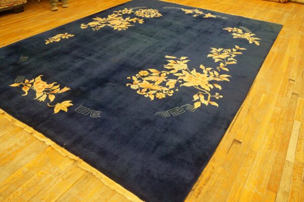 Large navy blue rug with gold and apricot floral motifs on a warm tone wood plank floor.