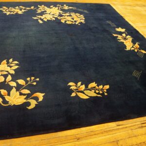 Large dark blue area rug with gold floral border pattern placed on bright hardwood floors.