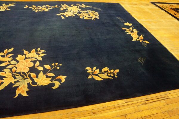 Large dark blue area rug with gold floral border pattern placed on bright hardwood floors.