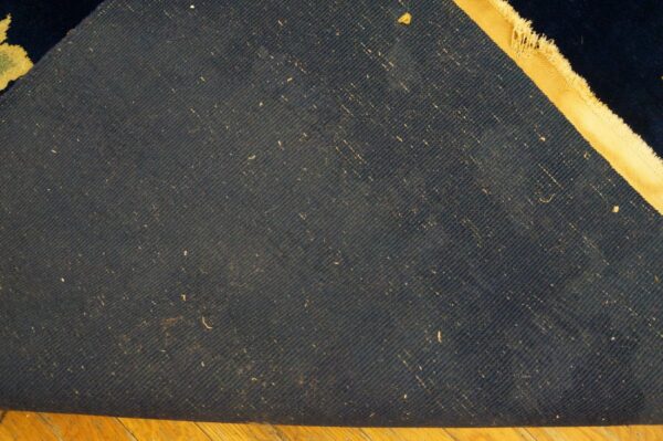Dark blue woven rug backing with diagonal lines and a tan edge folds over light wood flooring.