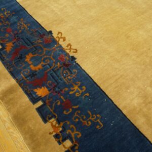 A golden-tan rug features a blue border with red and orange floral patterns on light wood flooring.