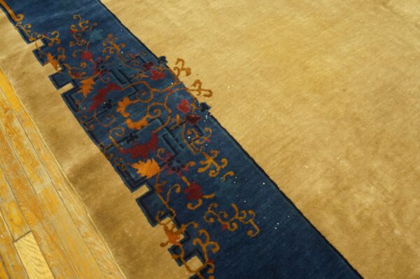 A golden-tan rug features a blue border with red and orange floral patterns on light wood flooring.