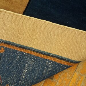 The tan woven backing of a blue and brown patterned rug is visible above glossy, worn hardwood floors.