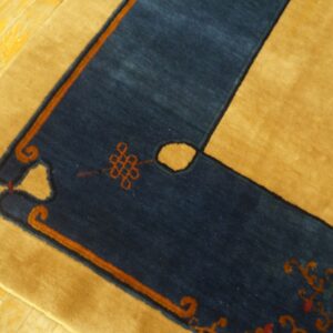 Navy blue and gold rug border with orange knot designs rests on a bright yellow plank floor.