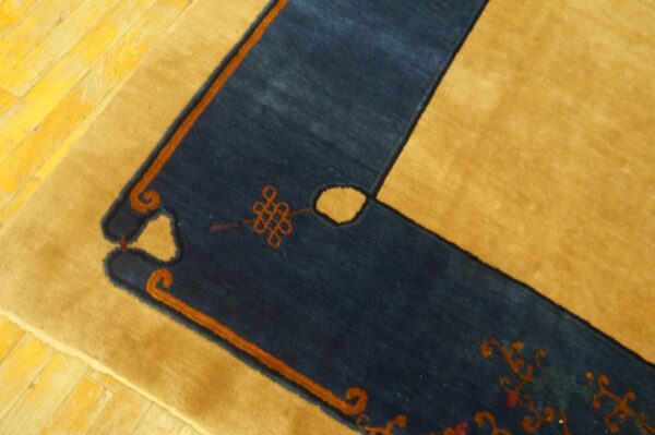 Navy blue and gold rug border with orange knot designs rests on a bright yellow plank floor.