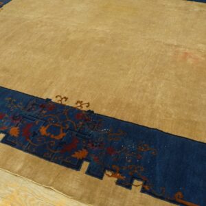 Tan area rug with a blue border, featuring rust and orange floral motifs, resting on light wood floors.