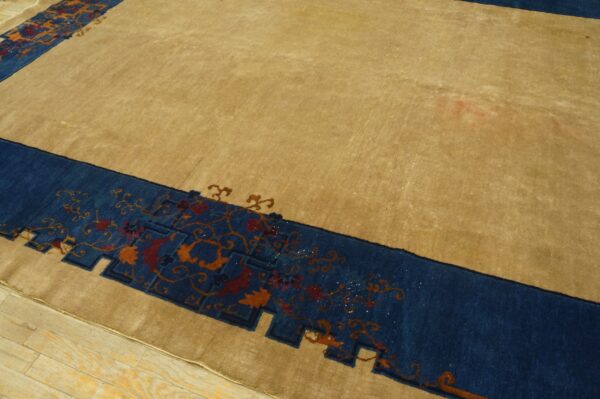 Tan area rug with a blue border, featuring rust and orange floral motifs, resting on light wood floors.
