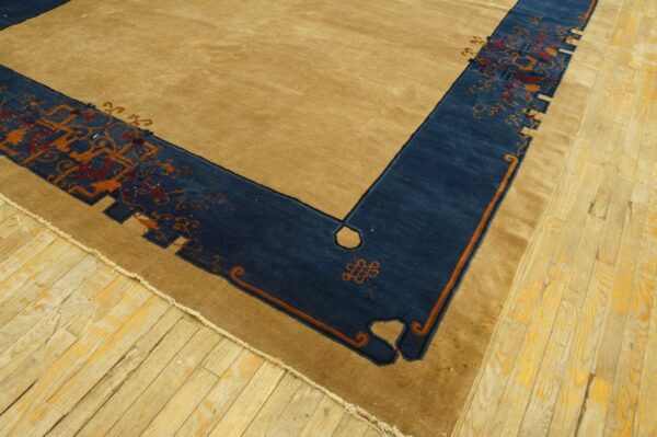 Tan rug featuring a wide, patterned dark blue border with orange and red details on wood floorboards.