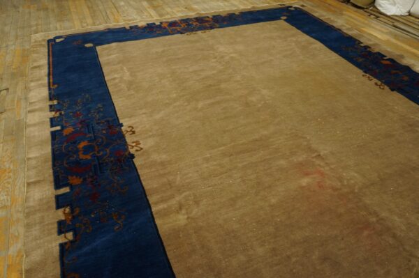 A large tan area rug features a thick blue border with intricate floral and gold scrollwork designs on a wood floor.