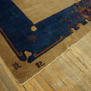 Tan rug with a navy border featuring rust motifs and black characters, resting on distressed wooden planks.