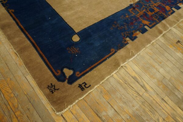 Tan rug with a navy border featuring rust motifs and black characters, resting on distressed wooden planks.