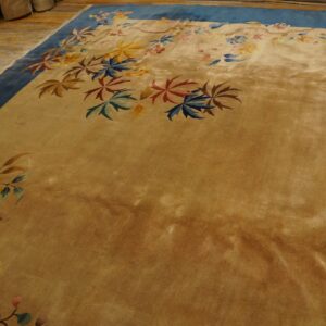 Velvety gold rug with wide blue borders and scattered colorful floral designs rests on rustic wood flooring.