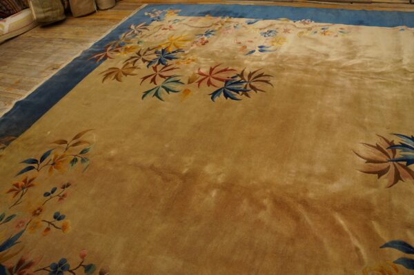Velvety gold rug with wide blue borders and scattered colorful floral designs rests on rustic wood flooring.