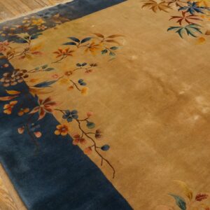 Golden rug with a wide blue border featuring multicolored floral and leaf designs on wooden floorboards.