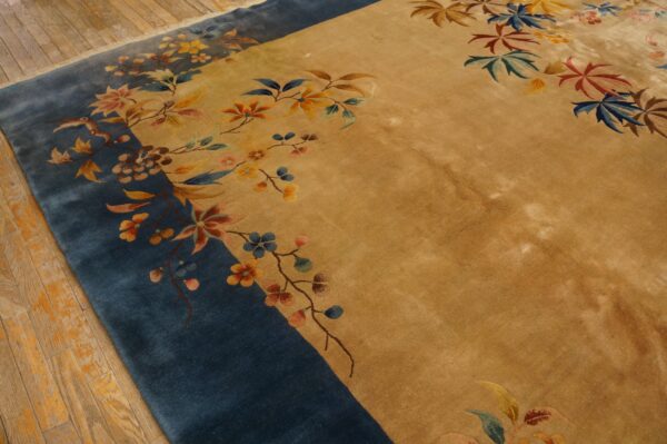 Golden rug with a wide blue border featuring multicolored floral and leaf designs on wooden floorboards.