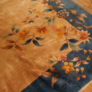 A close-up view of a gold and blue rug featuring detailed floral and vine patterns on wood flooring.