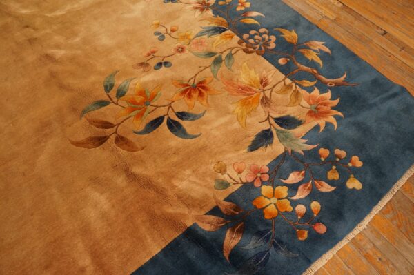 A close-up view of a gold and blue rug featuring detailed floral and vine patterns on wood flooring.