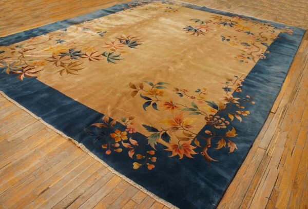 Plush golden tan rug featuring a scattered floral design with a wide dark blue border on wood floors.