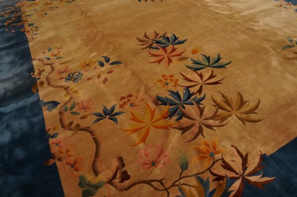 Tan rug closeup shows carved pink, orange, and blue stylized flowers, large leaves, and a deep blue edge.