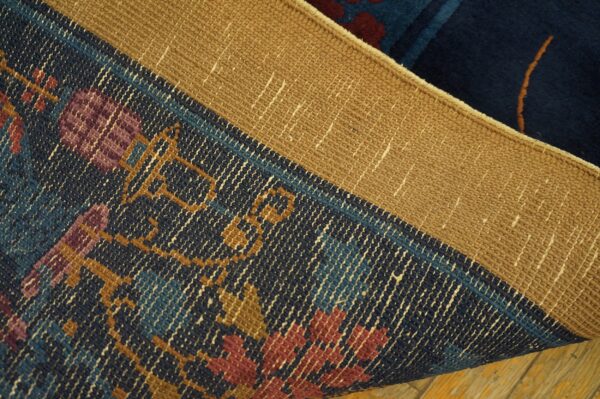 A curled navy rug exposes a woven tan backing and a patterned edge in gold, maroon, and blue.