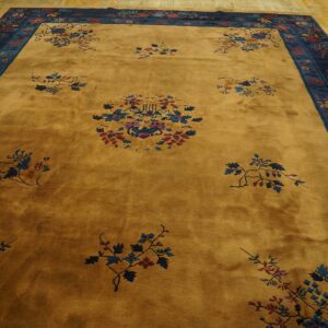 Gold rug featuring scattered blue and maroon florals, surrounded by a navy and teal ornamental border on wood flooring.