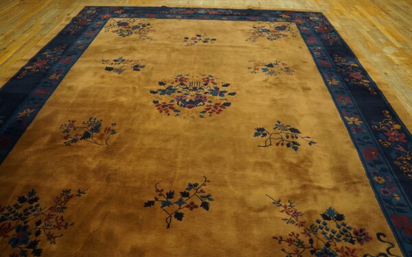 Gold rug featuring scattered blue and maroon florals, surrounded by a navy and teal ornamental border on wood flooring.