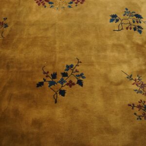 Golden ochre rug with scattered blue and red floral sprays, showing a visible blue border edge.