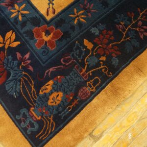 Navy rug corner with rust and blue florals, wide yellow border, resting on worn wooden floors.