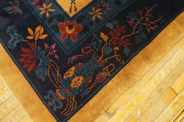Navy rug corner with rust and blue florals, wide yellow border, resting on worn wooden floors.