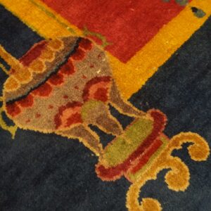 Detailed view of a rug showing a multi-colored ornamental design on navy, bordered by red and yellow.