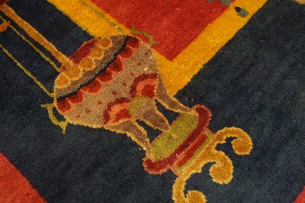 Detailed view of a rug showing a multi-colored ornamental design on navy, bordered by red and yellow.