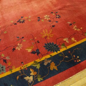 Red rug displaying colorful floral vines, framed by a thick navy blue and thin gold border on wood flooring.