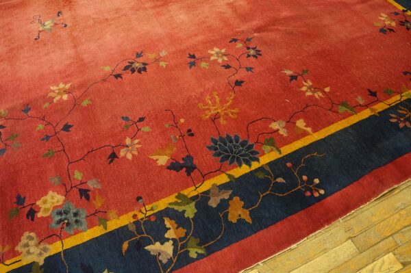 Red rug displaying colorful floral vines, framed by a thick navy blue and thin gold border on wood flooring.