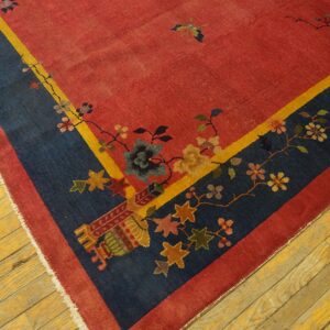 Red rug corner with a navy floral border, yellow trim, and exposed white fringe rests on distressed wood flooring.