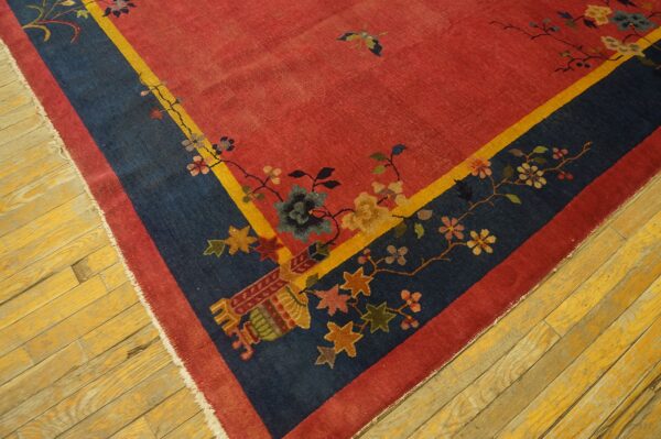Red rug corner with a navy floral border, yellow trim, and exposed white fringe rests on distressed wood flooring.