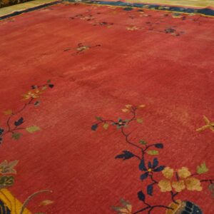 Red rug with low pile and scattered floral vines, featuring a navy and yellow border on a wood floor.